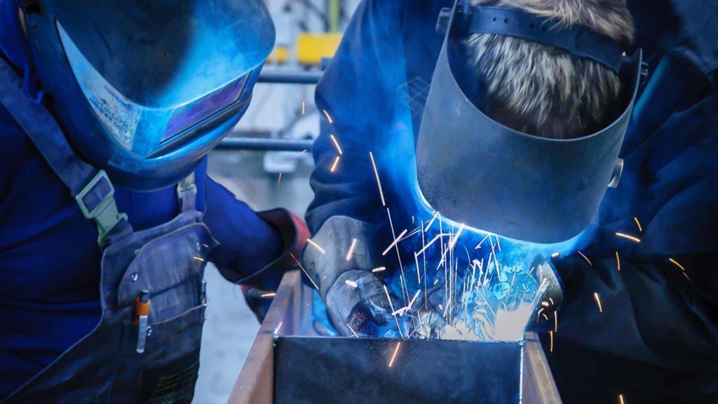A welding instructor and student practicing welding techniques