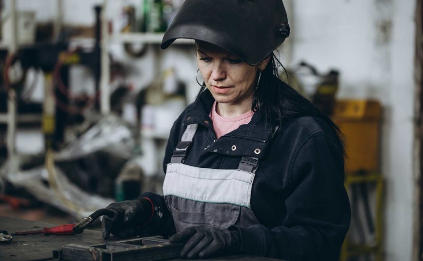 Torch in hand, a welder prepares her workpiece in an industrial shop.