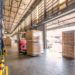 Warehouse workers operate forklifts and move boxes in a busy distribution environment.